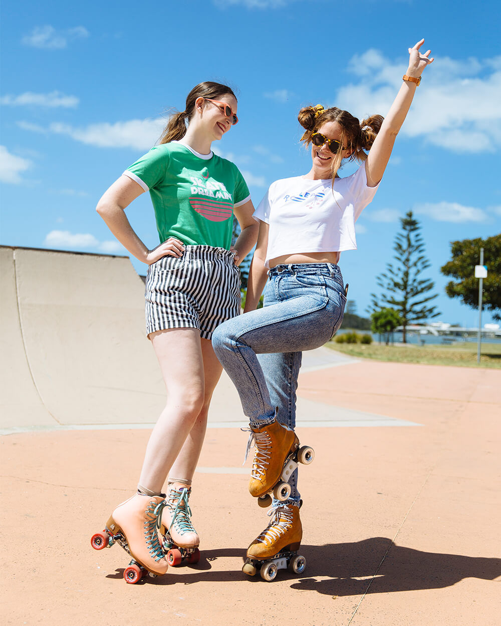 Amelia (left) and Stacey (right) wear roller skates posing at a skatepark by a lake.