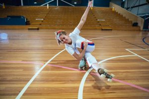 Stacey Skates wears an all white outfit and is doing a coffin on roller skates in a RollerFit class.