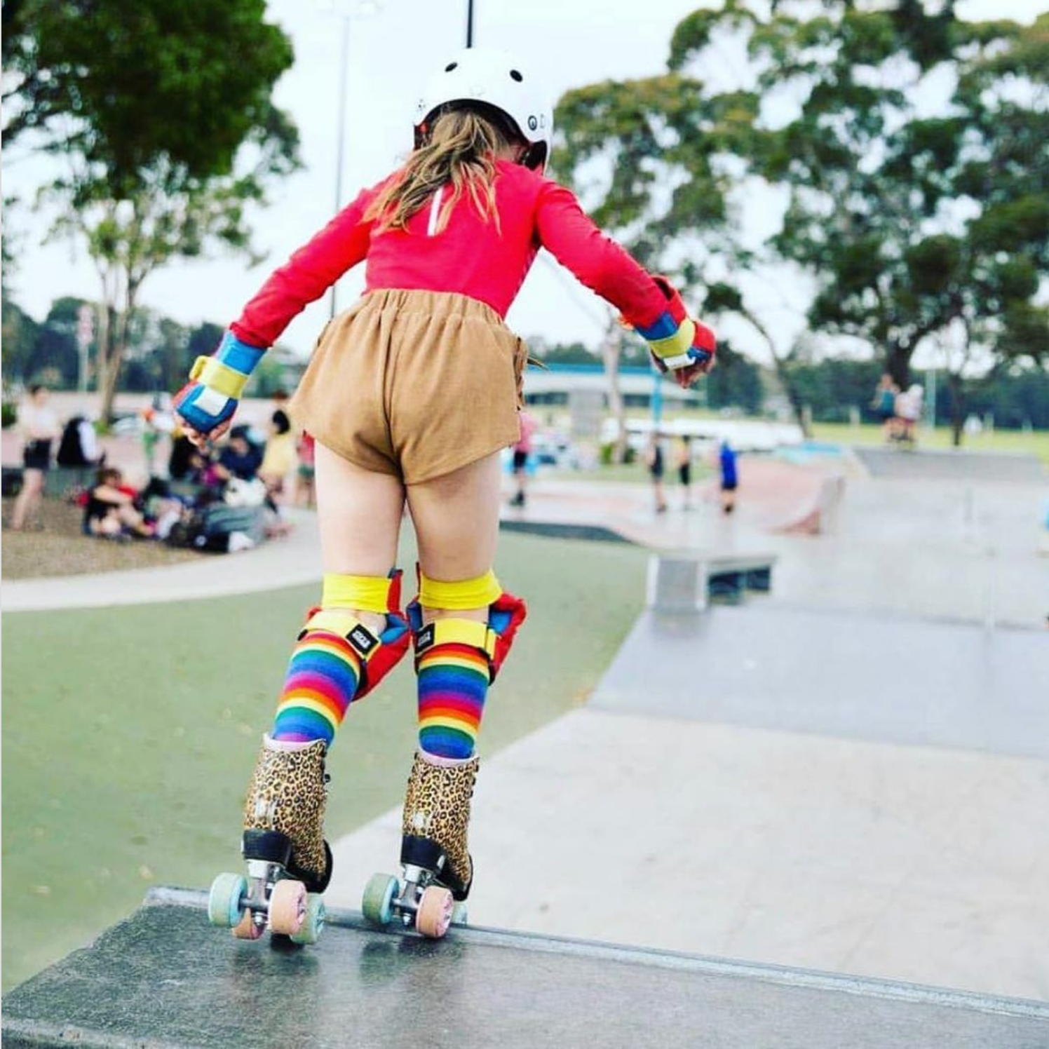 Willow, a young roller skater, is dropping in on a quarter pipe wearing roller skates and protective gear.