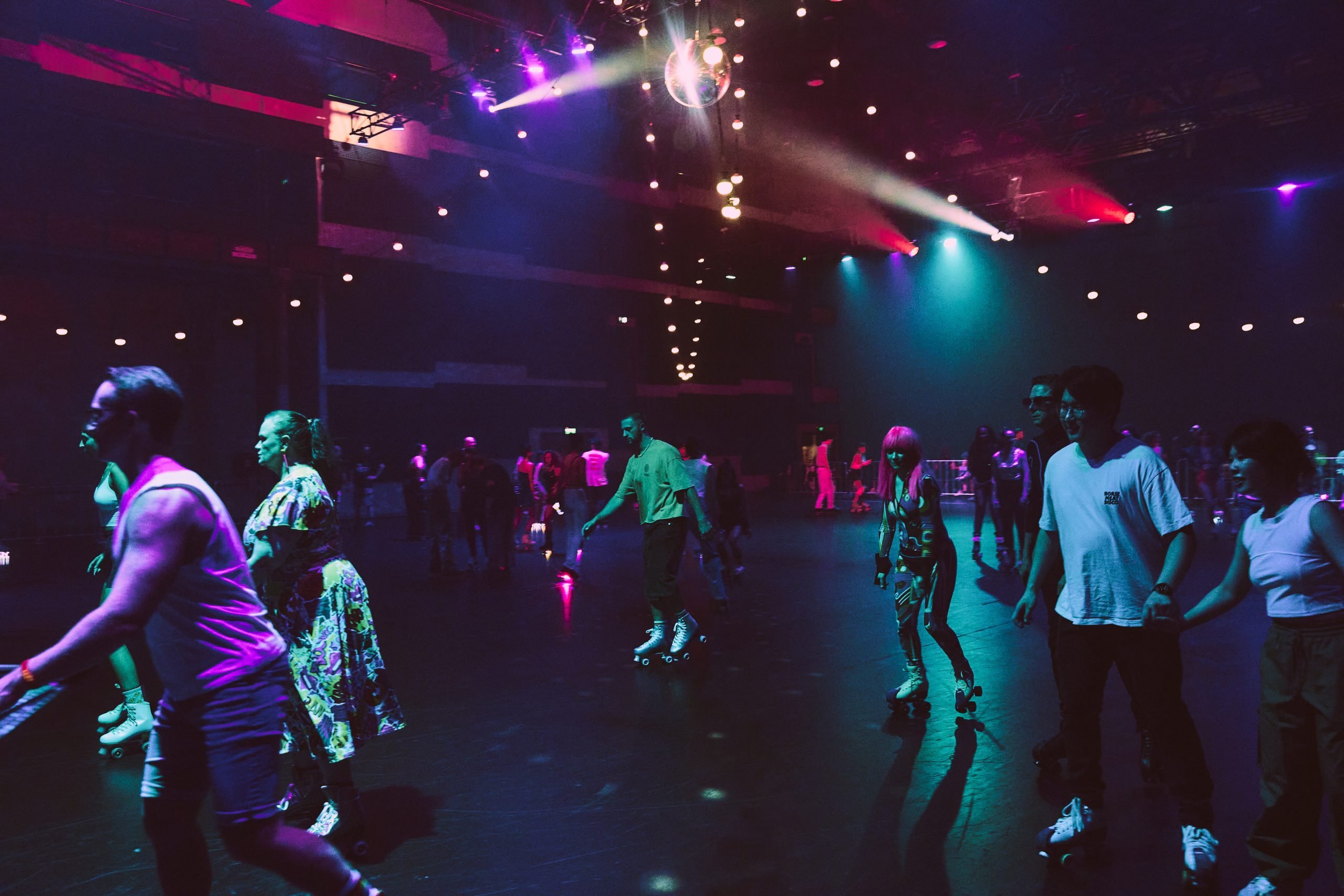 Roller skaters at a pop up rink at Carriageworks, Sydney. Rolling around under colourful lights and a big disco ball hanging in the centre of the rink.